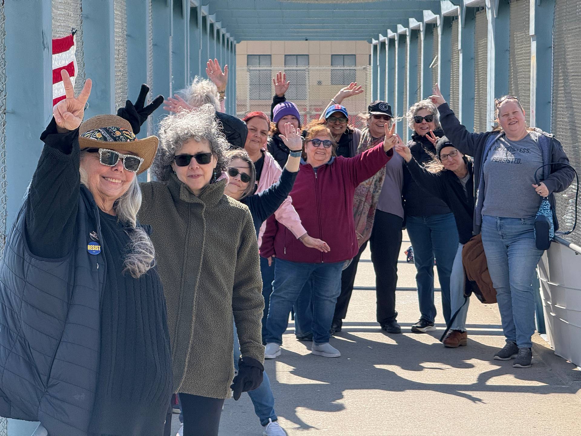 A group of happy protesters standing on a highway overpass smiling and holding up the peace sign on their fingers